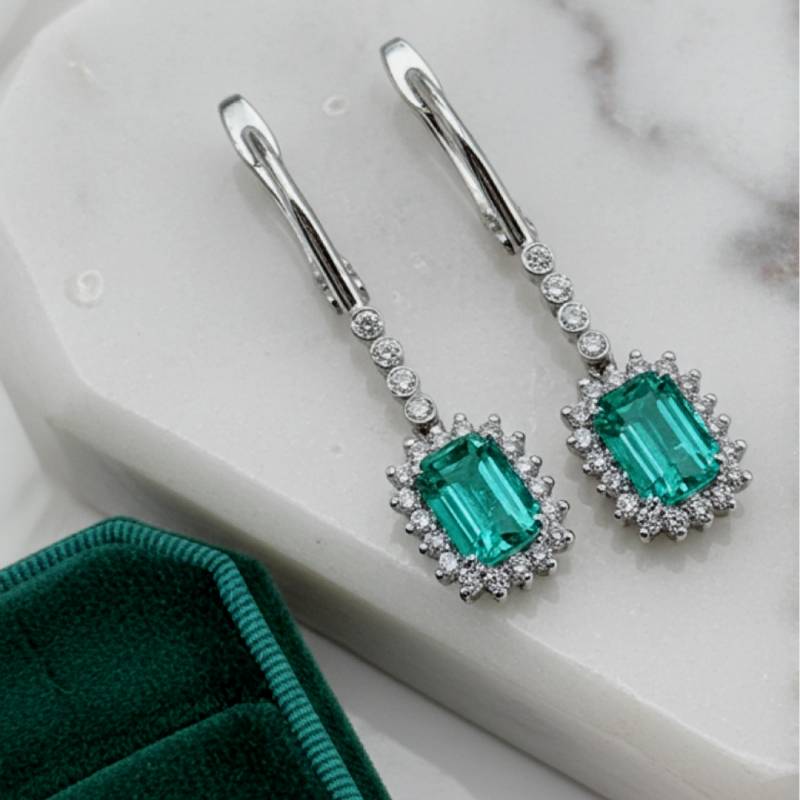 Emerald green gemstone earrings with silver accents on a marble surface.