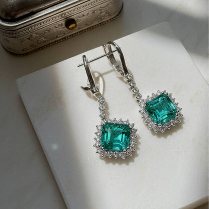 Pair of emerald green earrings with silver accents on a white surface.