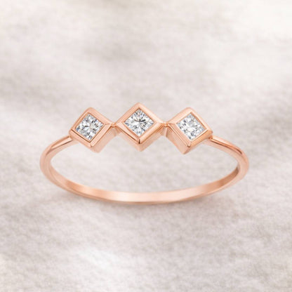 Rose gold ring with three diamonds on a light background