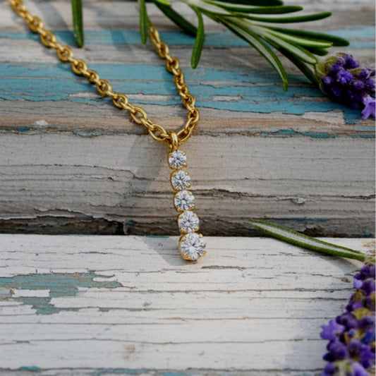 Gold necklace with diamond pendants on a rustic wooden surface with lavender flowers.