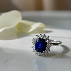 Ring with a blue gemstone and diamond accents on a white surface with a blurred background