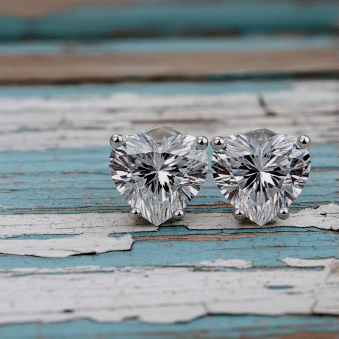 Heart-shaped diamond stud earrings on a rustic wooden surface