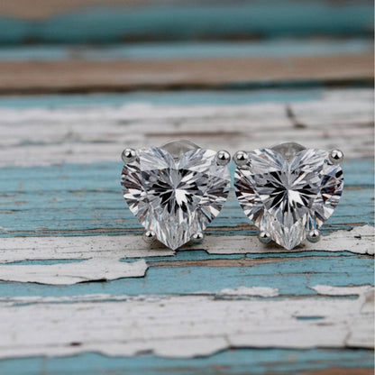 Heart-shaped diamond stud earrings on a rustic wooden surface