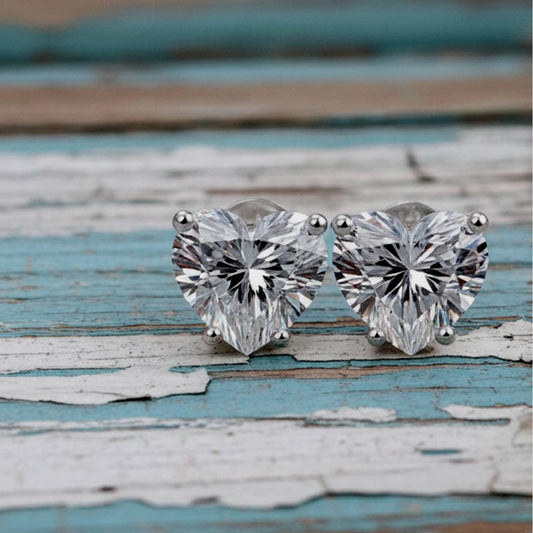 Heart-shaped diamond stud earrings on a rustic wooden surface