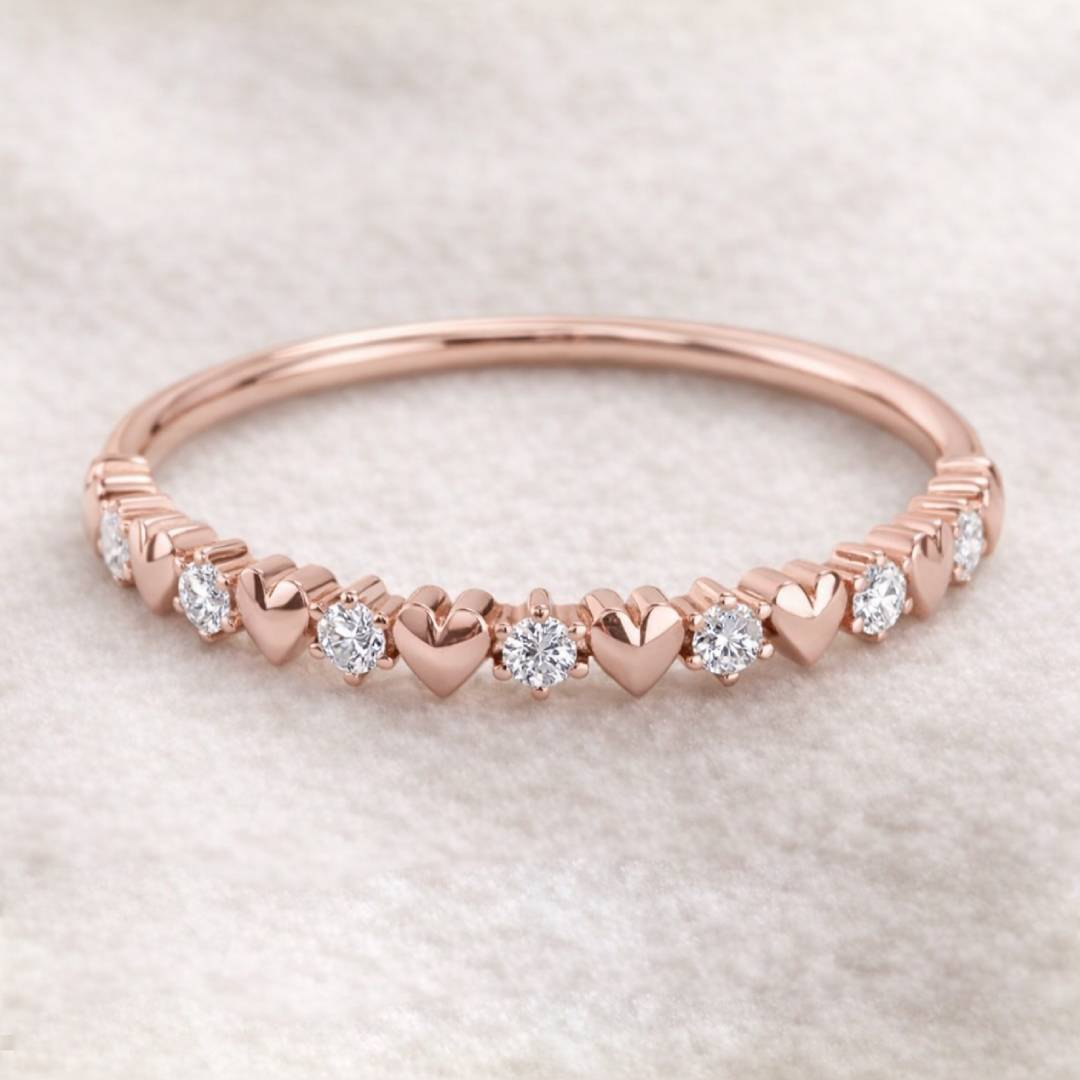 Rose gold ring with heart-shaped links and embedded diamonds on a light background