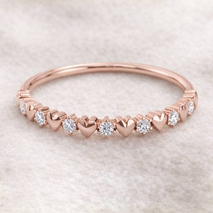 Rose gold ring with heart-shaped links and embedded diamonds on a light background