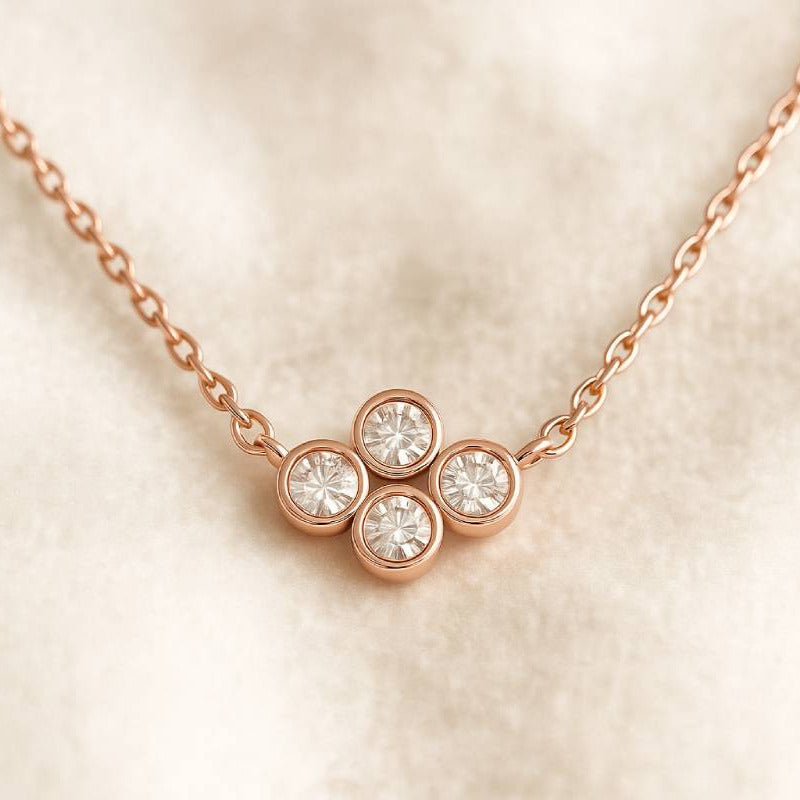 Rose gold necklace with four diamond-like stones on a beige background