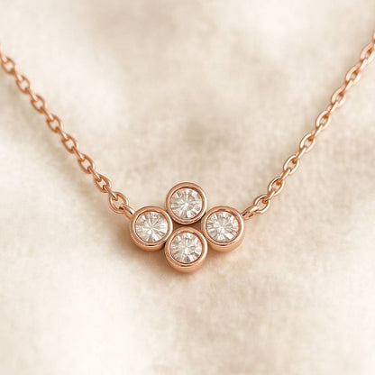 Rose gold necklace with four diamond-like stones on a beige background