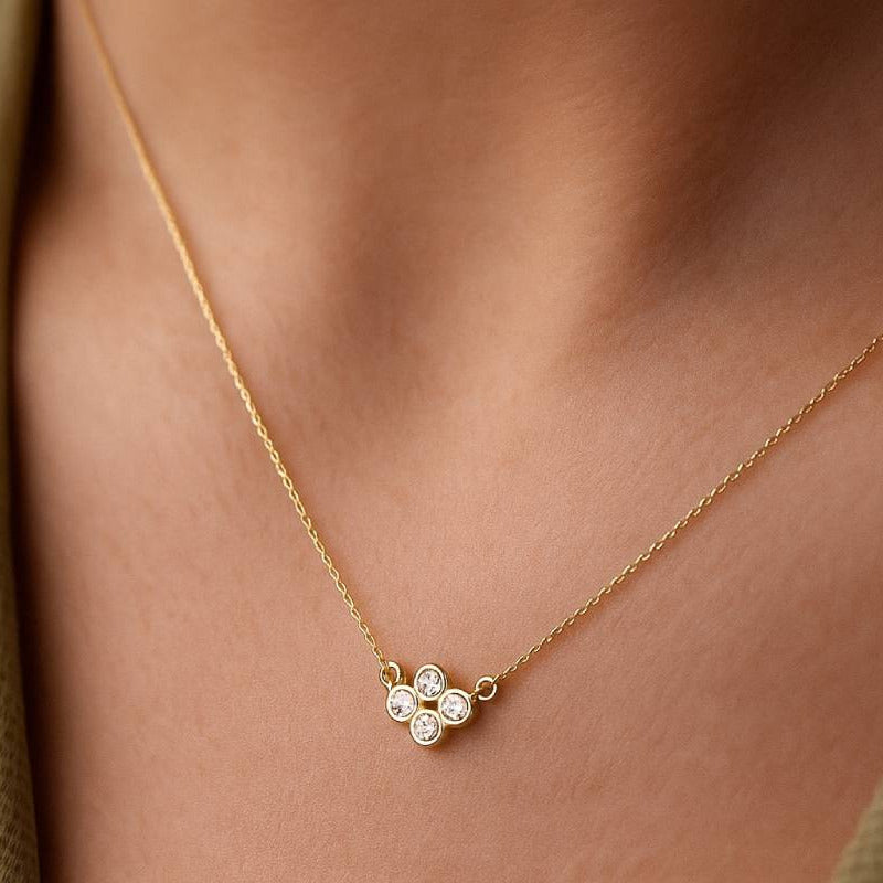 Gold necklace with a clover-shaped pendant on a person's neck
