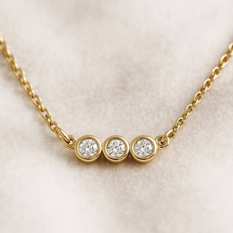 Gold necklace with three round diamonds on a light beige background