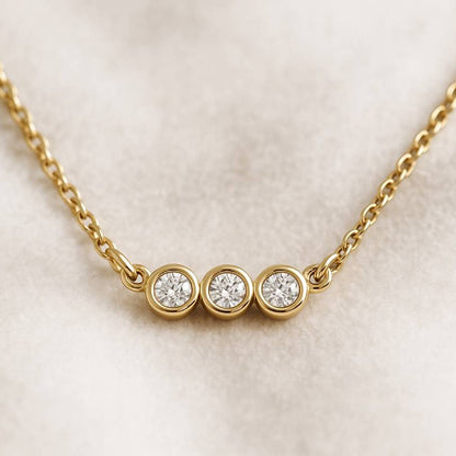 Gold necklace with three round diamonds on a light beige background
