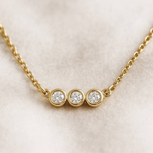 Gold necklace with three round diamonds on a light beige background