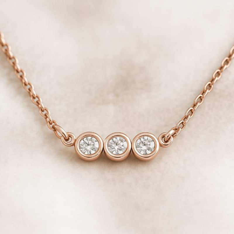 Rose gold necklace with three diamonds on a light beige background