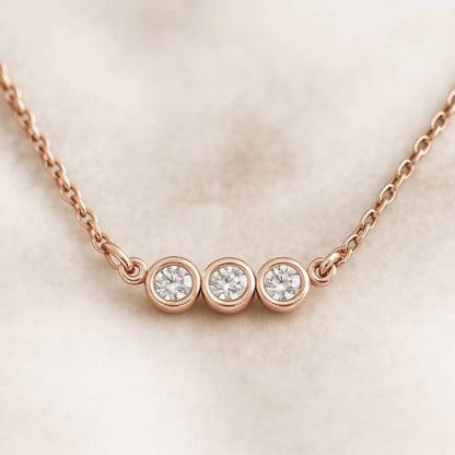 Rose gold necklace with three diamonds on a light beige background