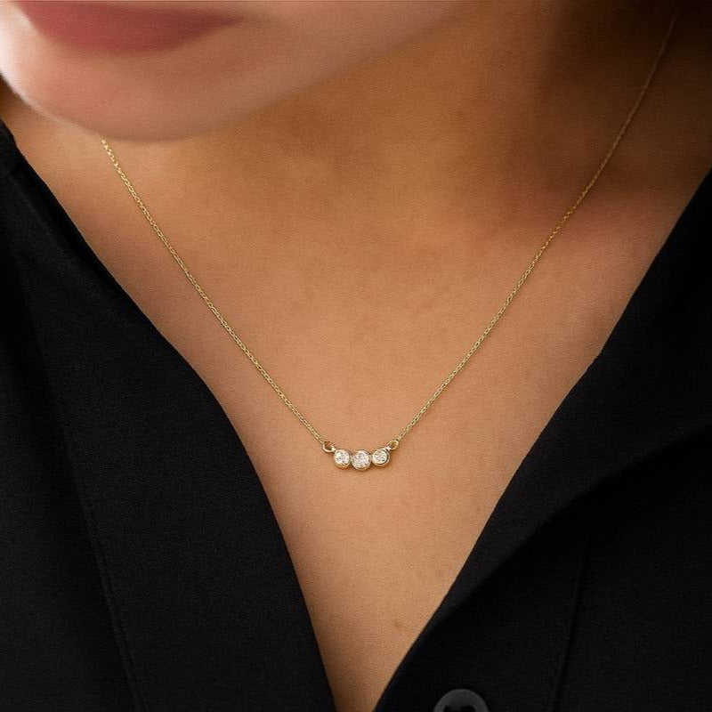Gold necklace with three diamonds on a person wearing a black top