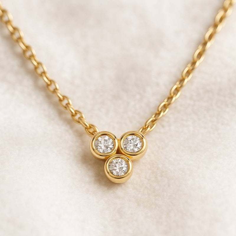 Gold necklace with three round diamonds on a light beige background