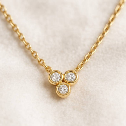 Gold necklace with three round diamonds on a light beige background