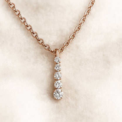 Rose gold necklace with diamond pendant on a soft beige background