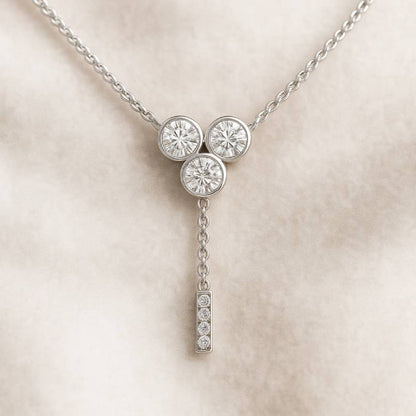 necklace with three round diamonds and a hanging bar on a beige background
