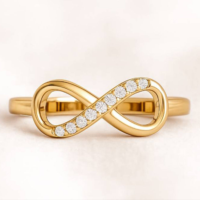 Gold infinity ring with diamonds on a light pink background