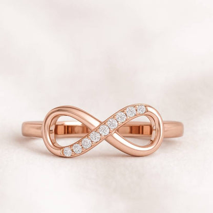 Rose gold infinity ring with diamonds on a light pink background