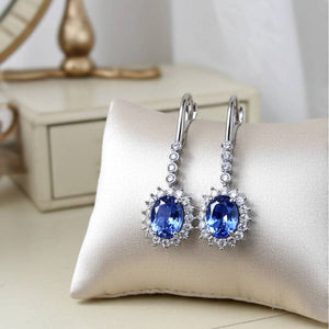 Pair of blue sapphire gemstone earrings on a white cushion with a neutral background