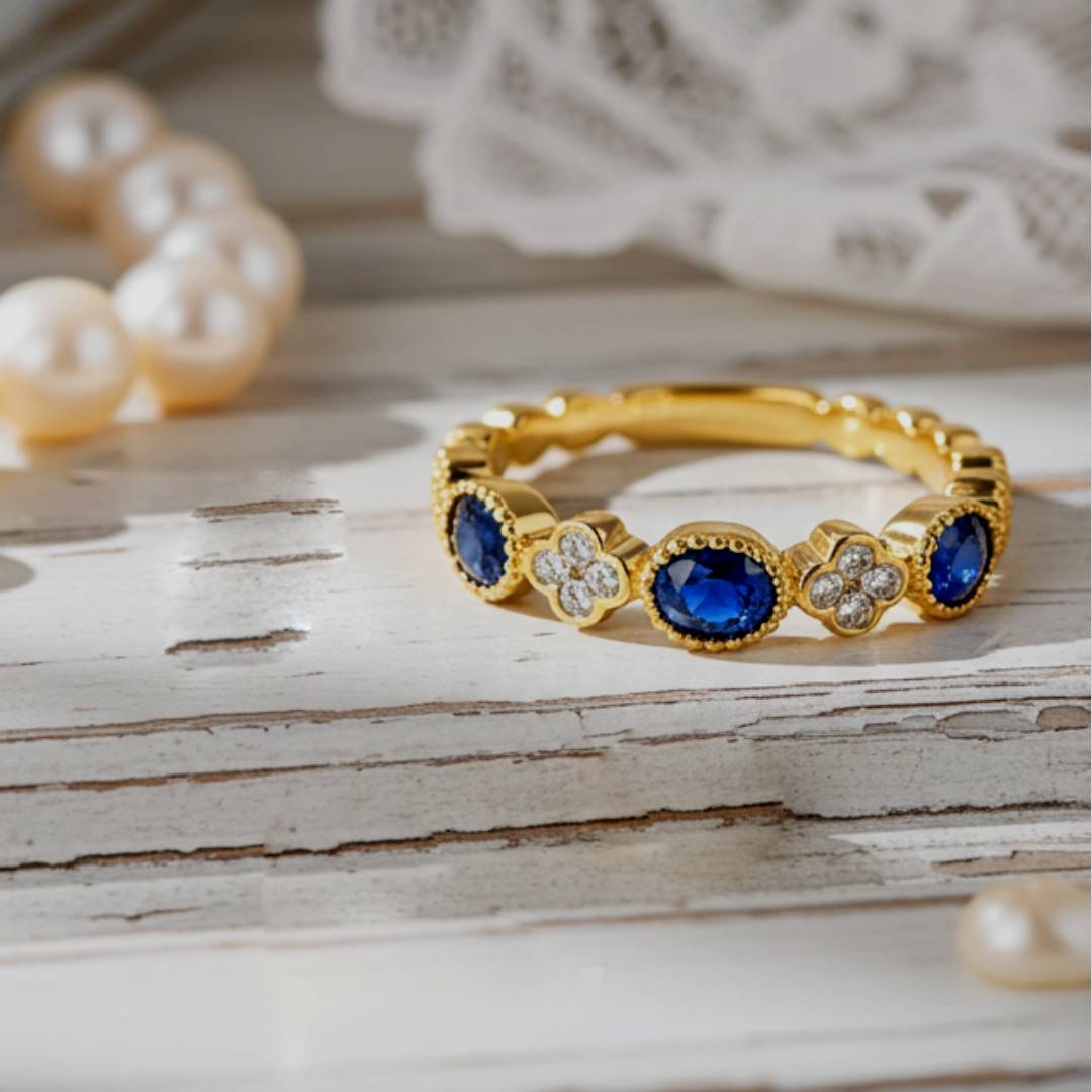 Gold ring with blue gemstones on a wooden surface with pearls in the background