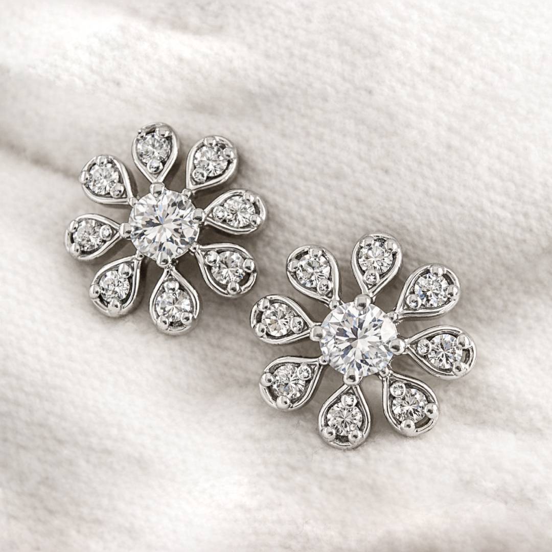 Pair of flower-shaped earrings with clear gemstones on a light fabric background