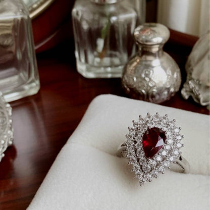 gold ring with a red gemstone on a white cushion, with decorative bottles in the background.