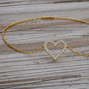 Gold bracelet with a heart-shaped clasp on a wooden surface