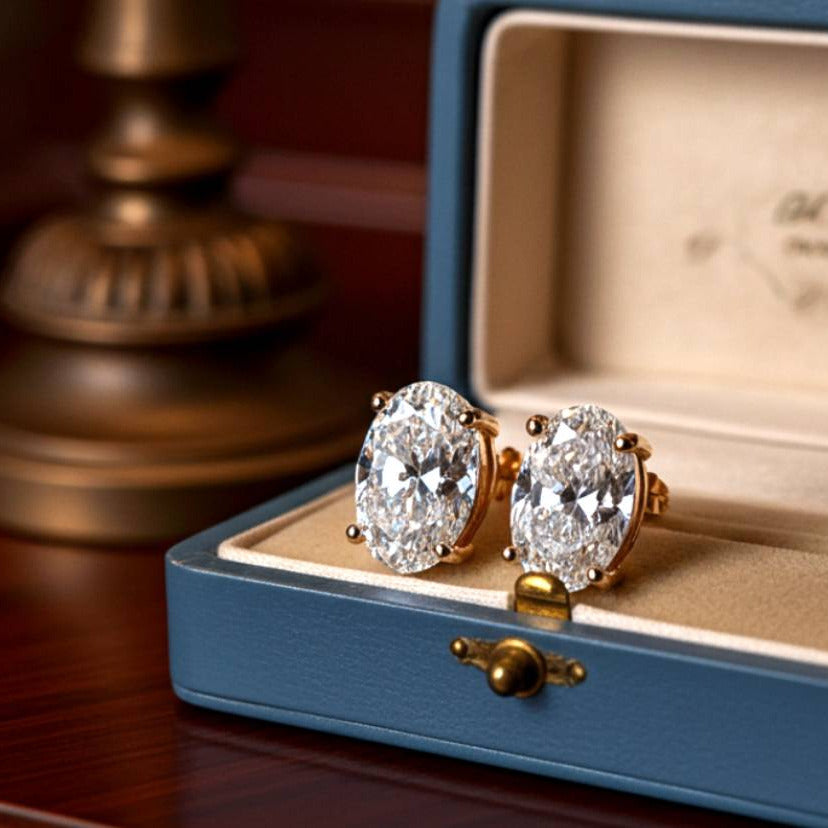Gold diamond earrings in an open jewelry box on a wooden surface.
