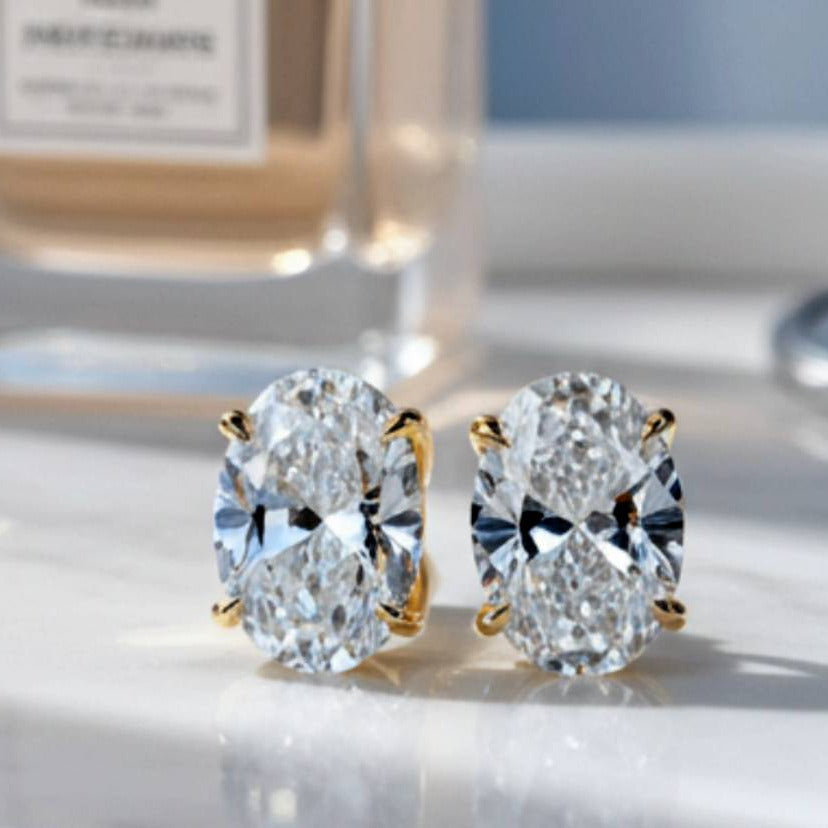 Gold earrings with large clear gemstones on a reflective surface, with a blurred background.