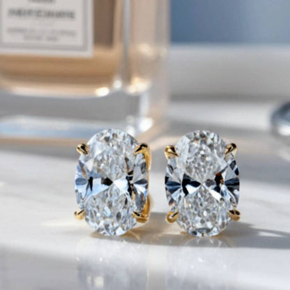 Gold earrings with large clear gemstones on a reflective surface, with a blurred background.